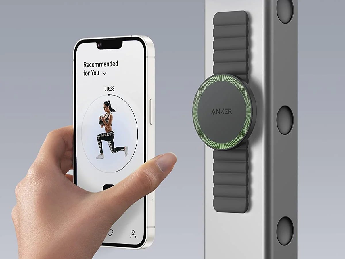 Hand holding a smartphone with an app displayed, next to a green Anker charging device.