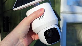 Hand holding a white security camera with a smartphone app interface above it.