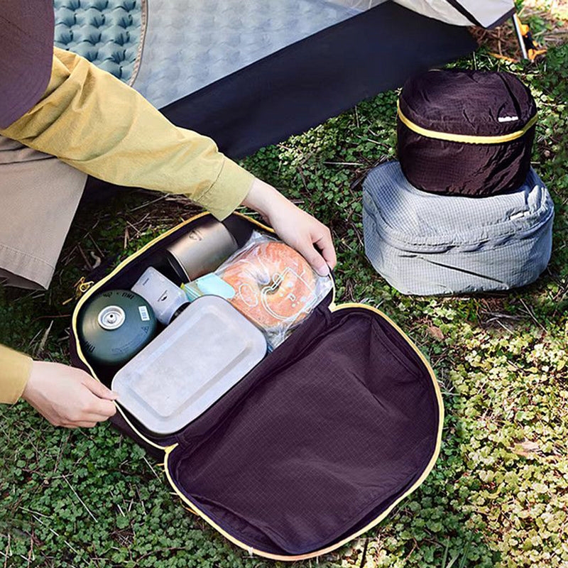 Person preparing a picnic outdoors with a portable cooler and food items.