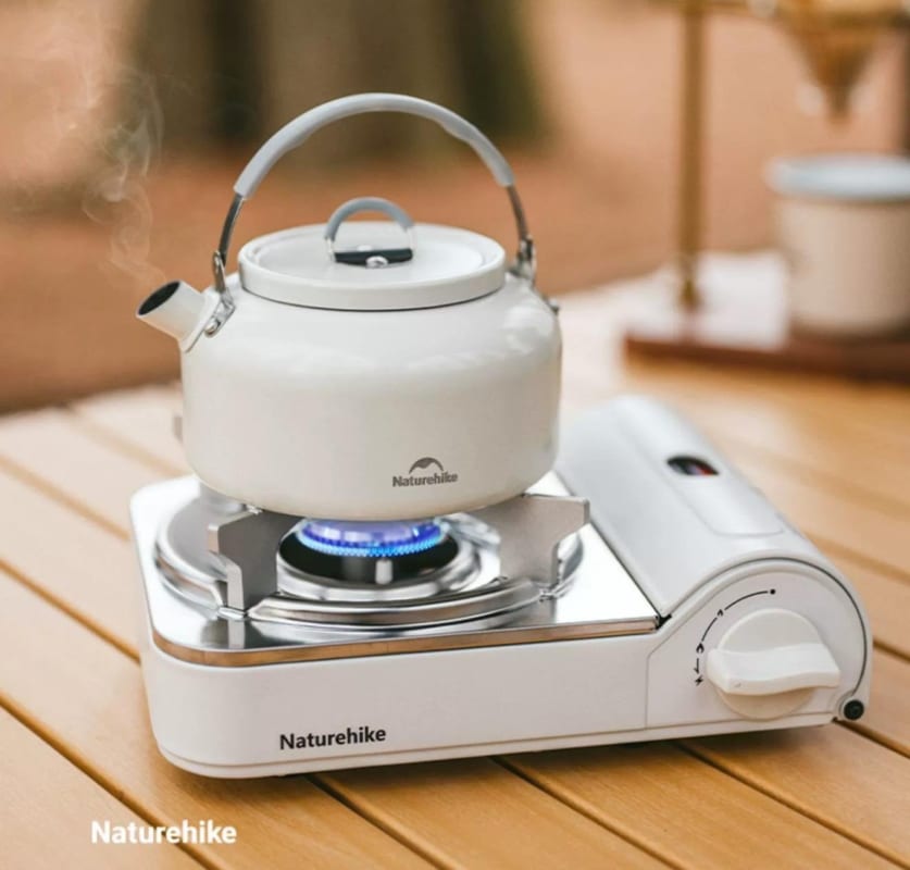 White kettle on a portable stove with 'Naturehike' branding, set against a blurred outdoor background.