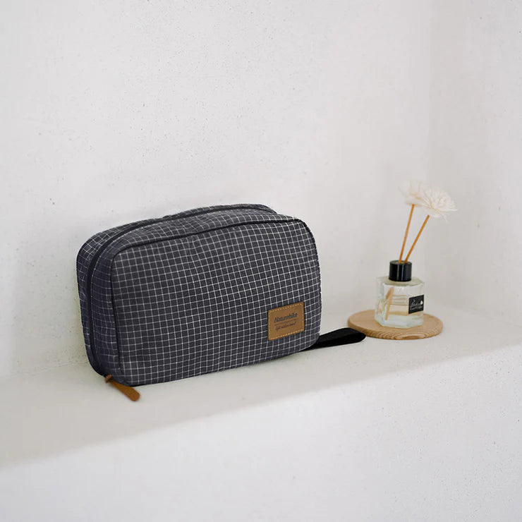 Gray checkered toiletry bag on a white surface with a small plant in the background