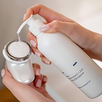 Person pouring a white liquid from a bottle into a container, with a focus on skincare products.