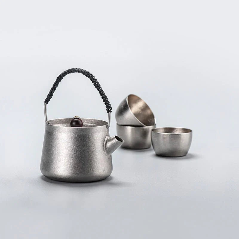 Silver teapot with a black handle and three matching silver cups on a light gray background