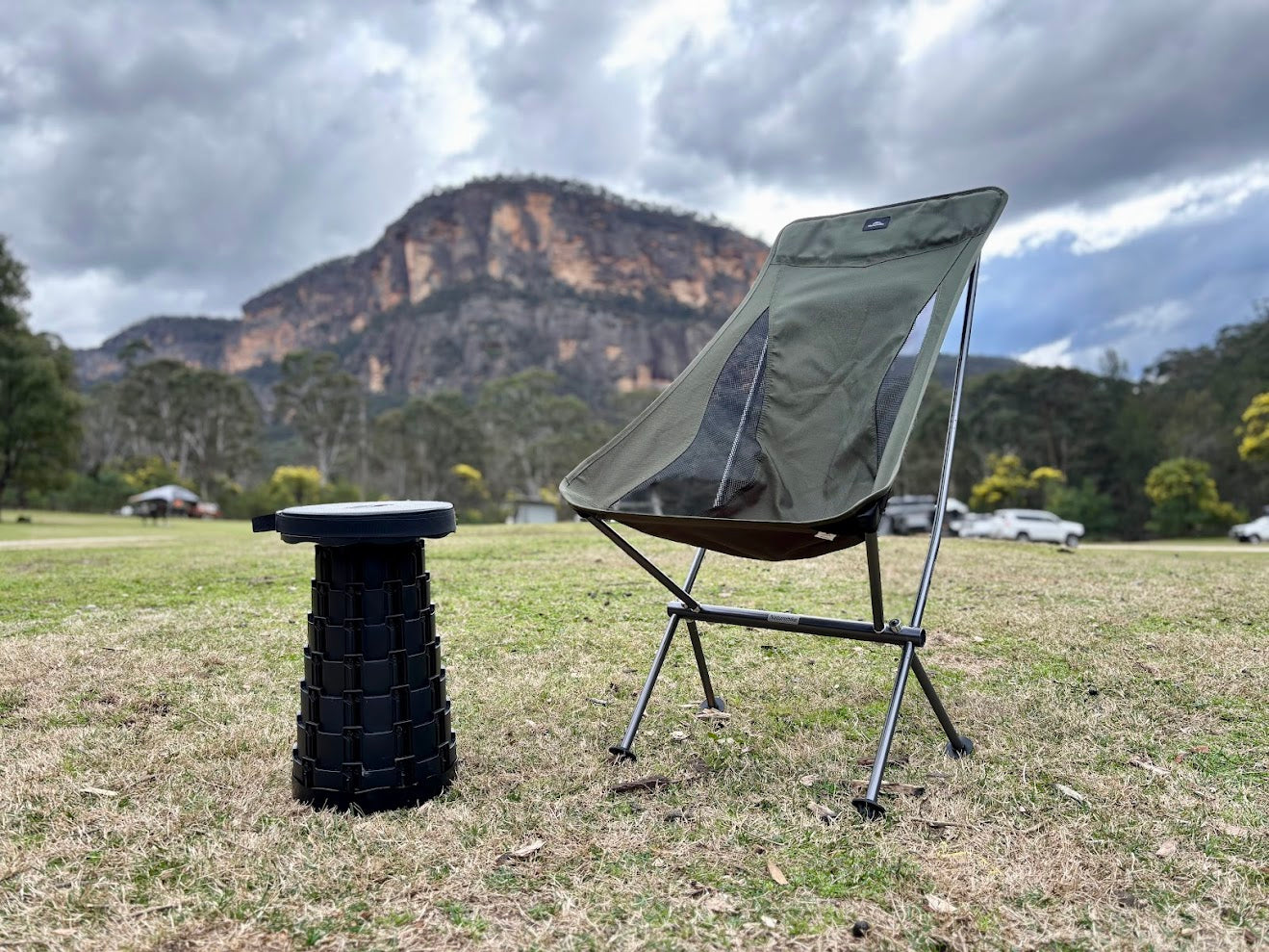 Portable chair and stool set on grass with mountains in the background